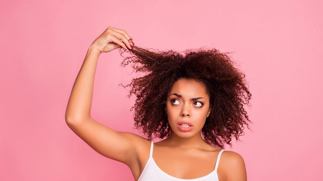 Girl stood in front of a pink background looking at her curly hair