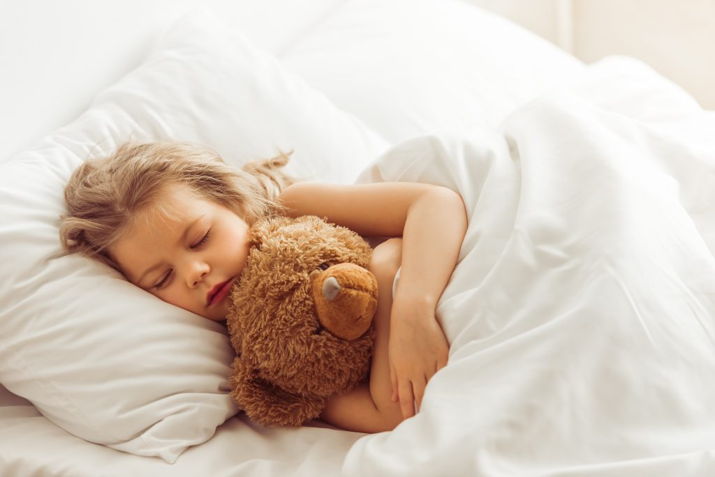 Sleeping little girl hugs teddy wrapped in her duvet