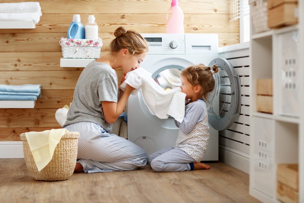 Happy family mother housewife and child daughter in laundry with washing machine