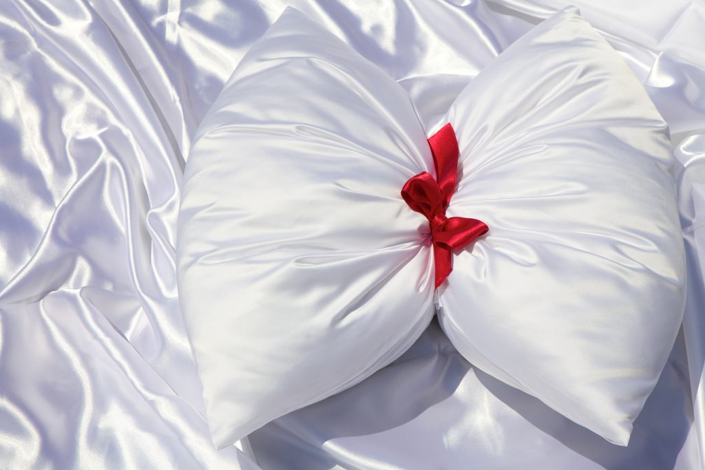 A white silk cushion with a red ribbon tied around it.