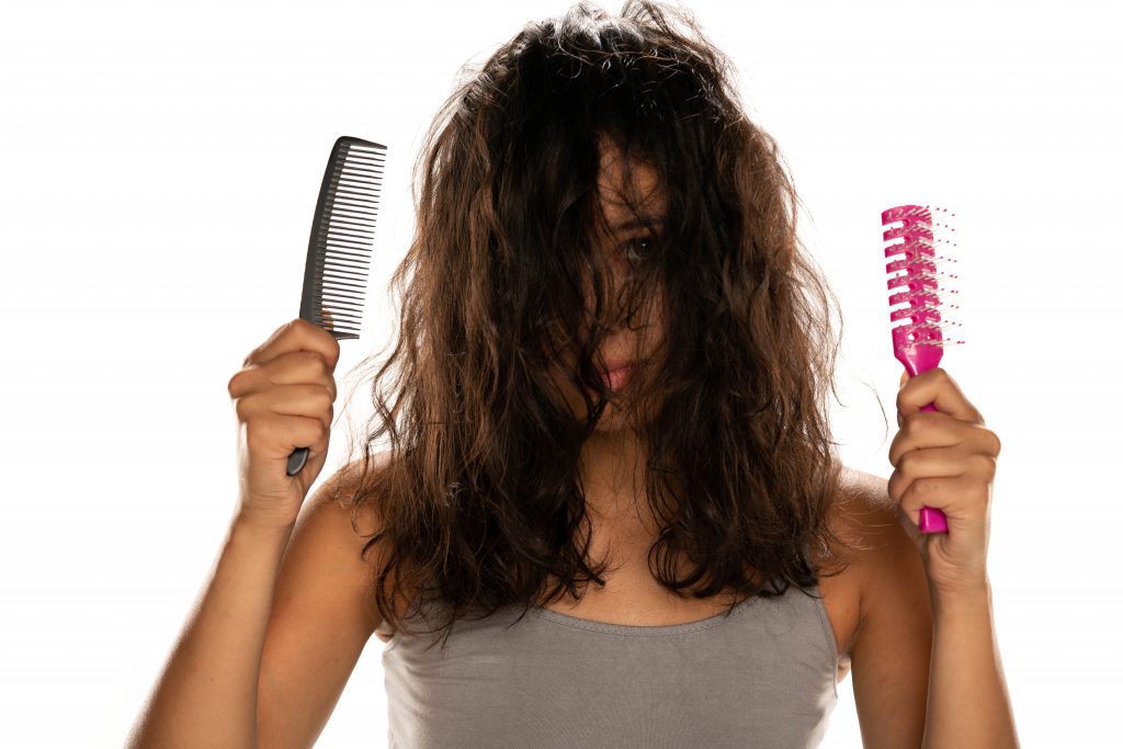 Girl with frizzy hair, a comb in her right hand and a hair brush in her left hand.