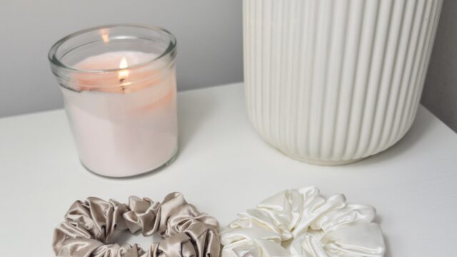 The Silk scruncies in pink, white and beige laid out on a white surface with a candle in the background.